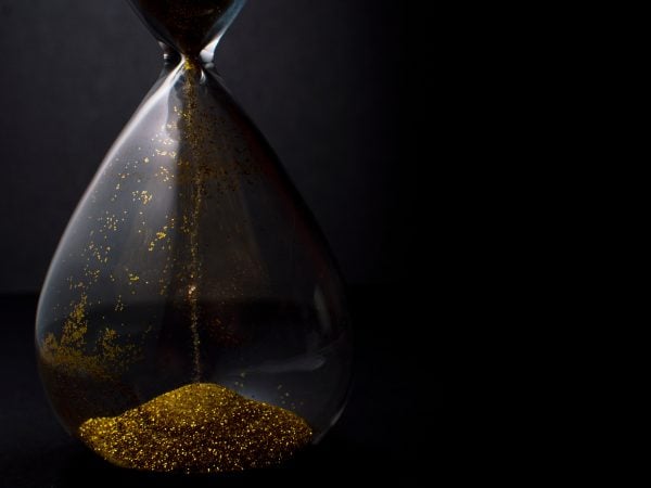 Sand and golden glitter passing through the glass bulbs of an hourglass