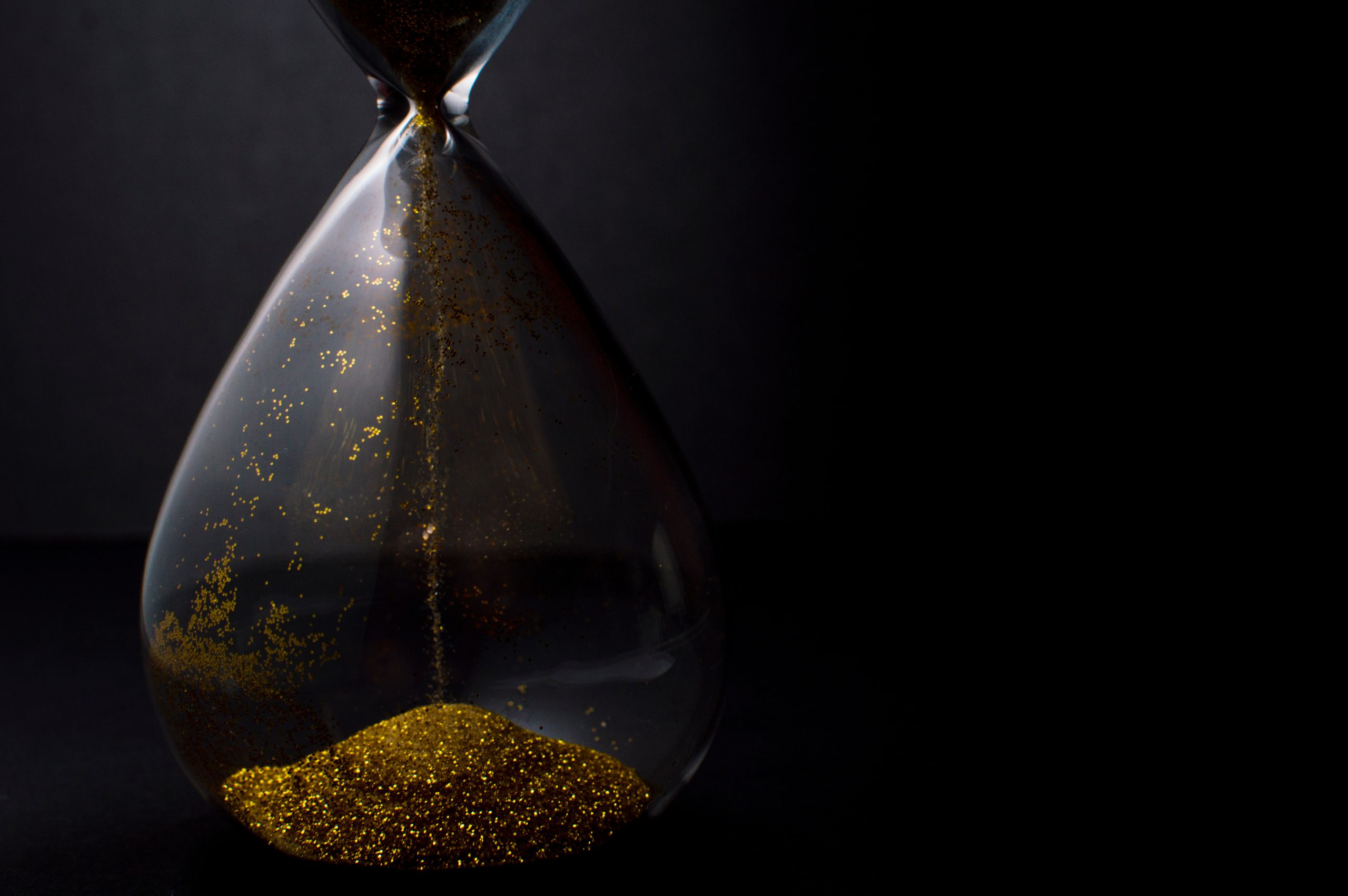 Sand and golden glitter passing through the glass bulbs of an hourglass